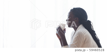 Pensive black girl drinking morning coffee against window and daydreaming Pensive black girl drinking morning coffee against window and daydreaming 59460528