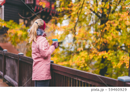 Adult blond woman holds a cup of herbal tee in hands on wooden bridge with beautiful golden autumn 59460929