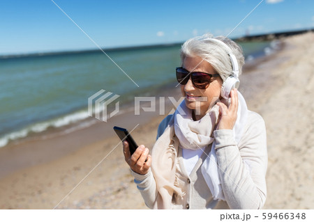 old woman in headphones with smartphone on beach old woman in headphones with smartphone on beach 59466348