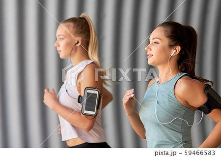 young women with earphones and smartphones running 59466583