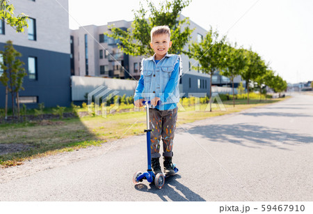 happy little boy riding scooter in city 59467910