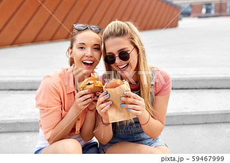 teenage girls or friends eating burgers outdoors 59467999
