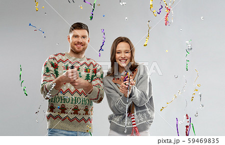 couple in christmas sweaters popping party poppers 59469835