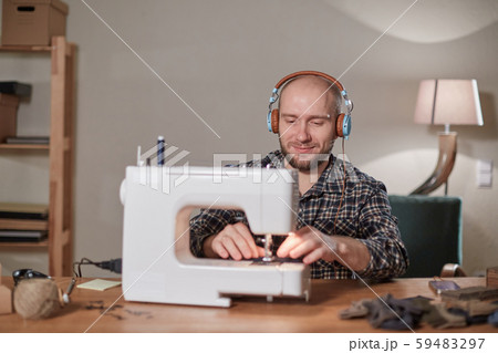Happy man listen music and working with sewing machine in a textile studio. Tailor makes bow ties of 59483297