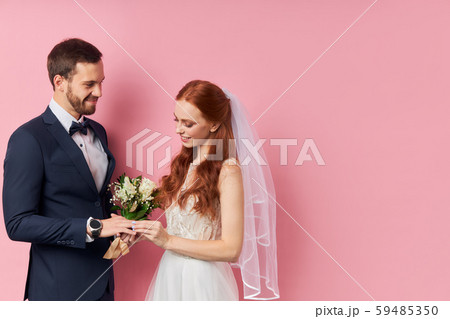Trendy gentleman in tuxedo with bow putting ring on the bride s finger Trendy gentleman in tuxedo with bow putting ring on the bride s finger 59485350