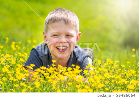 A boy with a smile is resting on a green lawn with yellow wildflowers A boy with a smile is resting on a green lawn with yellow wildflowers 59486064