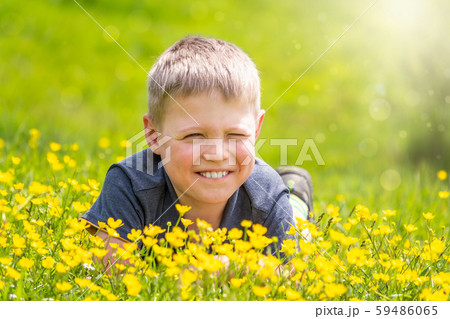 A boy with a smile is resting on a green lawn with yellow wildflowers A boy with a smile is resting on a green lawn with yellow wildflowers 59486065