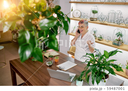 Top view on mature woman florist talking on phone standing around plants Top view on mature woman florist talking on phone standing around plants 59487001