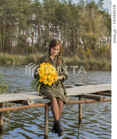 Beautiful girl with a bouquet of yellow roses. Effective woman near the river. Pretty Woman. Teen girl with yellow roses. Girl on the old bridge. 59489036