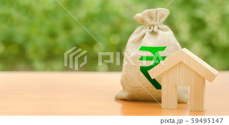 Wooden house figurine and a money bag with a Indian rupee symbol. Mortgage loan for the purchase of housing. Down payment first installment on the loan. Buying and selling, valuation of real estate. 59495147