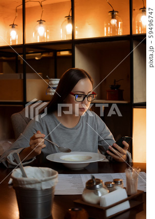 Woman eating soup and browsing smartphone in cafe 59496747