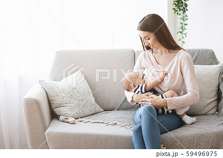 Millennial mom nursing her infant baby on sofa at home Millennial mom nursing her infant baby on sofa at home 59496975