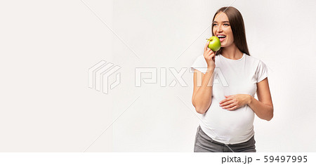 Expectant Woman Eating Apple Touching Belly Standing In Studio, Panorama 59497995