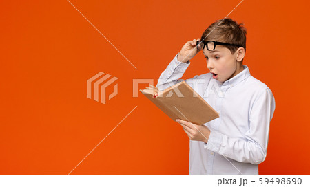Emotional teenager reading exciting book, raising his glasses in amazement Emotional teenager reading exciting book, raising his glasses in amazement 59498690