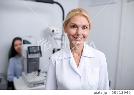 Blonde-haired pleasant eye doctor wearing white coat smiling Blonde-haired pleasant eye doctor wearing white coat smiling 59512949