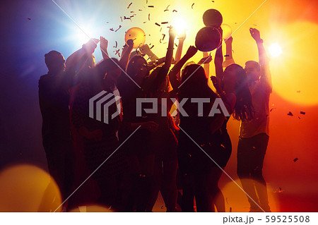 A crowd of people in silhouette raises their hands against colorful neon light on party background A crowd of people in silhouette raises their hands against colorful neon light on party background 59525508