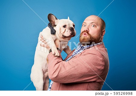 Bald male in jacket with french bulldog in his arms on empty blue background Bald male in jacket with french bulldog in his arms on empty blue background 59526998