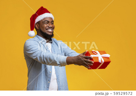 Cheerful black delivery guy in Santa hat giving gift box Cheerful black delivery guy in Santa hat giving gift box 59529572
