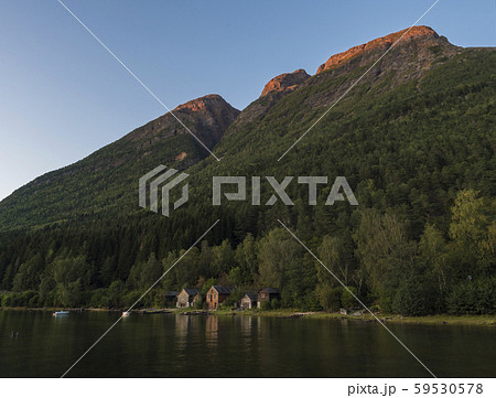 View of traditional wooden cottage along Hardanger Fjord in Kinsarvik in Norway with forest rocky 59530578