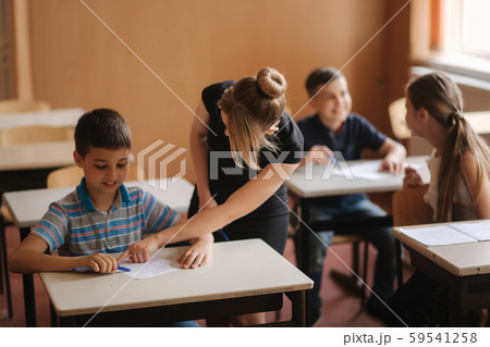 Teacher helping school kids writing test in classroom. education, elementary school, learning and Teacher helping school kids writing test in classroom. education, elementary school, learning and 59541258