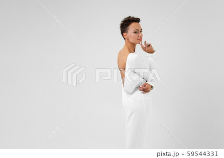 A young beautiful girl with short dark hair, in a long white dress with her back open stands back to 59544331