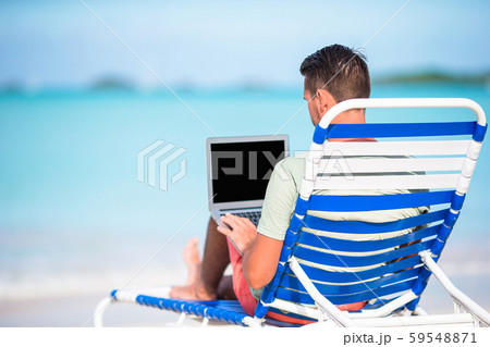 Young man with laptop on tropical caribbean beach. Man sitting on the sunbed with computer and 59548871