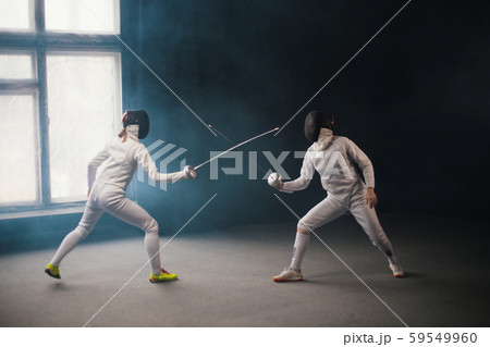 A fencing training - two women in protective costumes having a duel A fencing training - two women in protective costumes having a duel 59549960