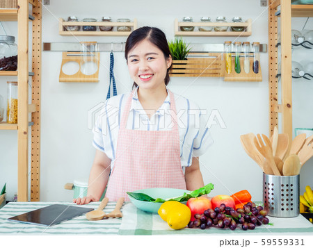 Asian woman in kitchen.smile teeth girl wearing pin apron with fruit and tablet on table prepare healthy food feeling happy Asian woman in kitchen.smile teeth girl wearing pin apron with fruit and tablet on table prepare healthy food feeling happy 59559331