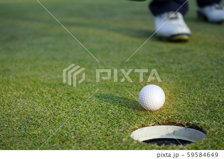 White golf ball near hole on green grass. White golf ball near hole on green grass. 59584649