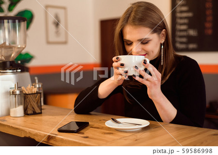 Smiling woman in a good mood enjoy cup of coffee sitting in a cafe. Smiling woman in a good mood enjoy cup of coffee sitting in a cafe. 59586998