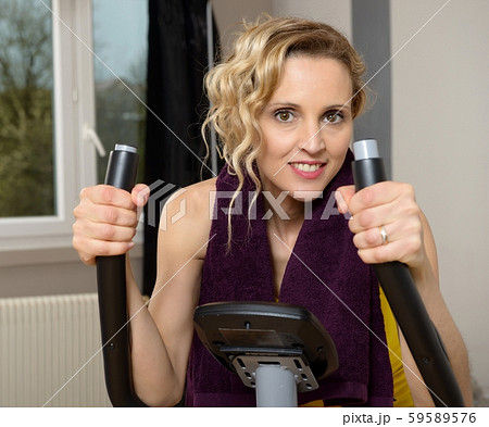 Fit woman on exercise bike at home Fit woman on exercise bike at home 59589576