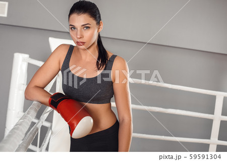 Boxing. Woman boxer in gloves leaning on rope on ring smiling confident Boxing. Woman boxer in gloves leaning on rope on ring smiling confident 59591304