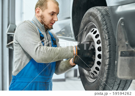 Side view of auto mechanic tighten bolts of car's wheel 59594262