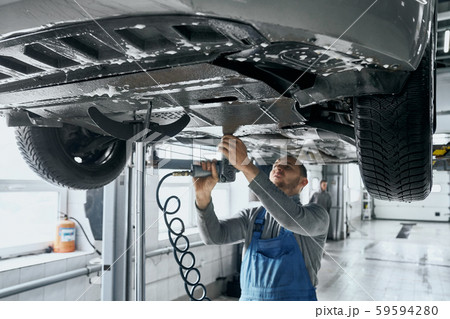 Competent mechanic in blue overalls repairing car suspension Competent mechanic in blue overalls repairing car suspension 59594280