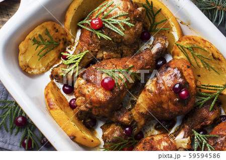 Baked chicken drumstick with oranges and cranberries in a baking sheet on a wooden background. Christmas food Table with decorations. 59594586