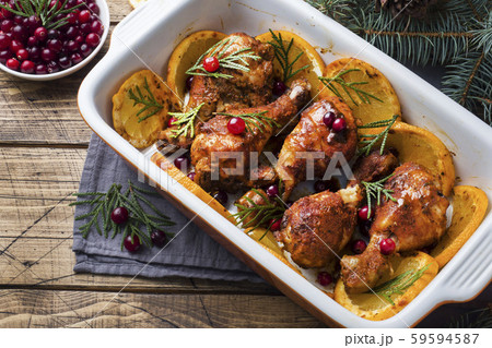 Baked chicken drumstick with oranges and cranberries in a baking sheet on a wooden background. Christmas food Table with decorations. 59594587