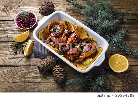 Baked chicken drumstick with oranges and cranberries in a baking sheet on a wooden background. Christmas food Table with decorations. 59594588
