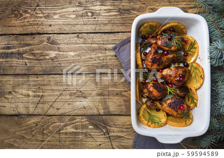 Baked chicken drumstick with oranges and cranberries in a baking sheet on a wooden background. Christmas food Table with decorations. 59594589