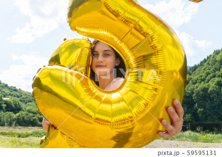 Teen girl looking through golden balloons in camera Teen girl looking through golden balloons in camera 59595131
