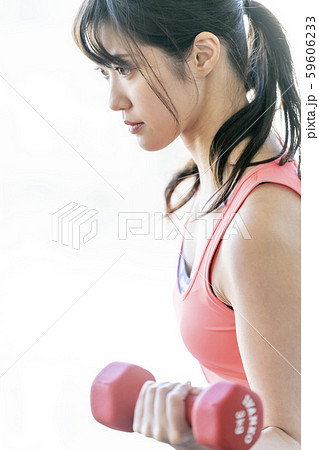 ダンベルで腕の筋肉上腕三頭筋を鍛える真剣な表情の若い女性の写真素材