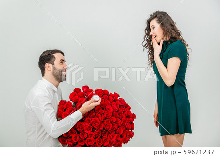 Man asking partner to marry him by giving her a engagement ring and bunch of red flowers, woman is 59621237
