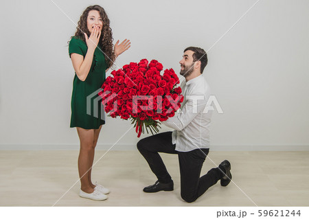 Man asking partner to marry him by giving her a engagement ring and bunch of red flowers, woman is 59621244