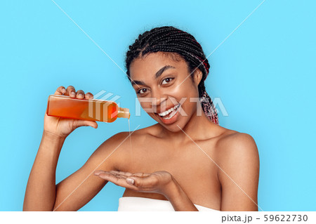 Beauty Concept. Young african woman isolated on blue pouring shampoo into hand smiling joyful 59622730