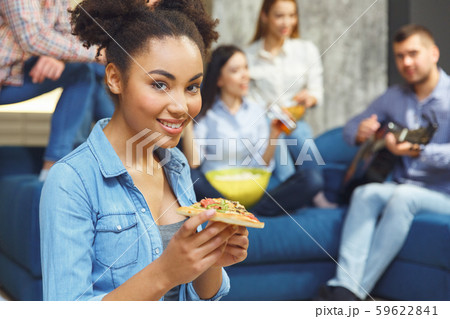 Group of friends having party indoors fun together african descent girl sitting close-up with pizza 59622841