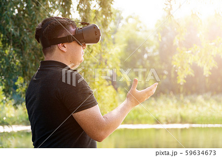 Smile happy man getting experience using VR-headset glasses of virtual reality in nature summer Smile happy man getting experience using VR-headset glasses of virtual reality in nature summer 59634673
