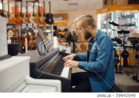 Musician trying to play on piano in music store 59642049