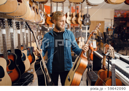 Young guy choosing acoustic guitar in music store 59642090