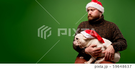 Man and dog in santa caps on empty green background in studio. Man and dog in santa caps on empty green background in studio. 59648637