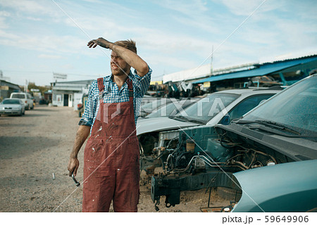 Tired repairman with wrench on car junkyard Tired repairman with wrench on car junkyard 59649906