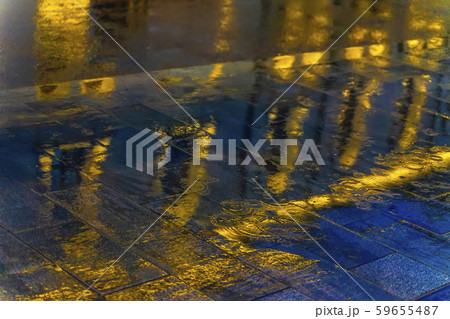 Blurred reflection of a bright building in a puddle on the asphalt. Rain in the city at night Blurred reflection of a bright building in a puddle on the asphalt. Rain in the city at night 59655487